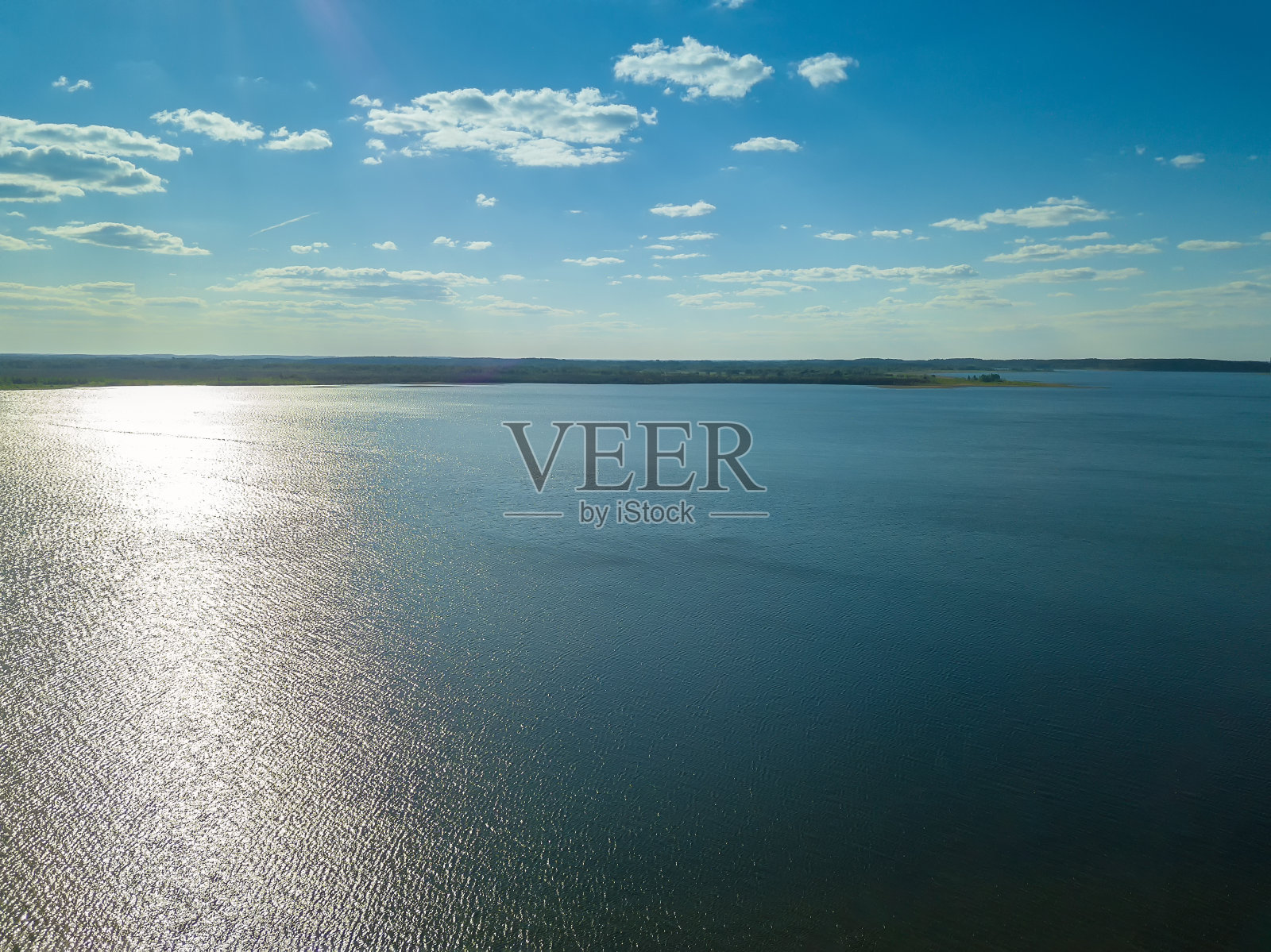 从无人机上看到的是一个蓝色的湖，反射着太阳和远处绿色的森林。在一个阳光明媚的日子里，无人机拍摄的美丽风景照片摄影图片