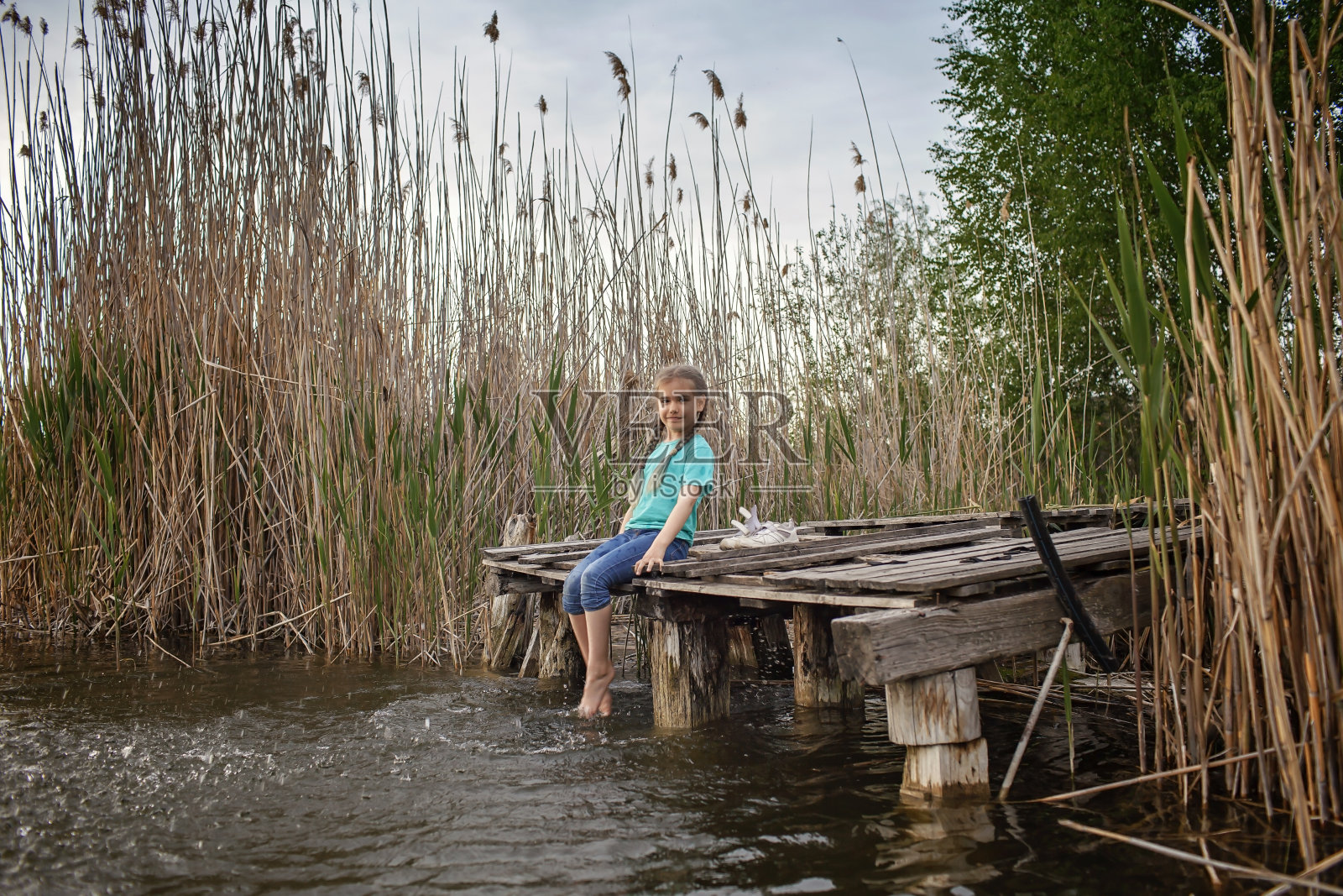 快乐的女孩在湖边的码头上用腿戏水，快乐的童年照片摄影图片