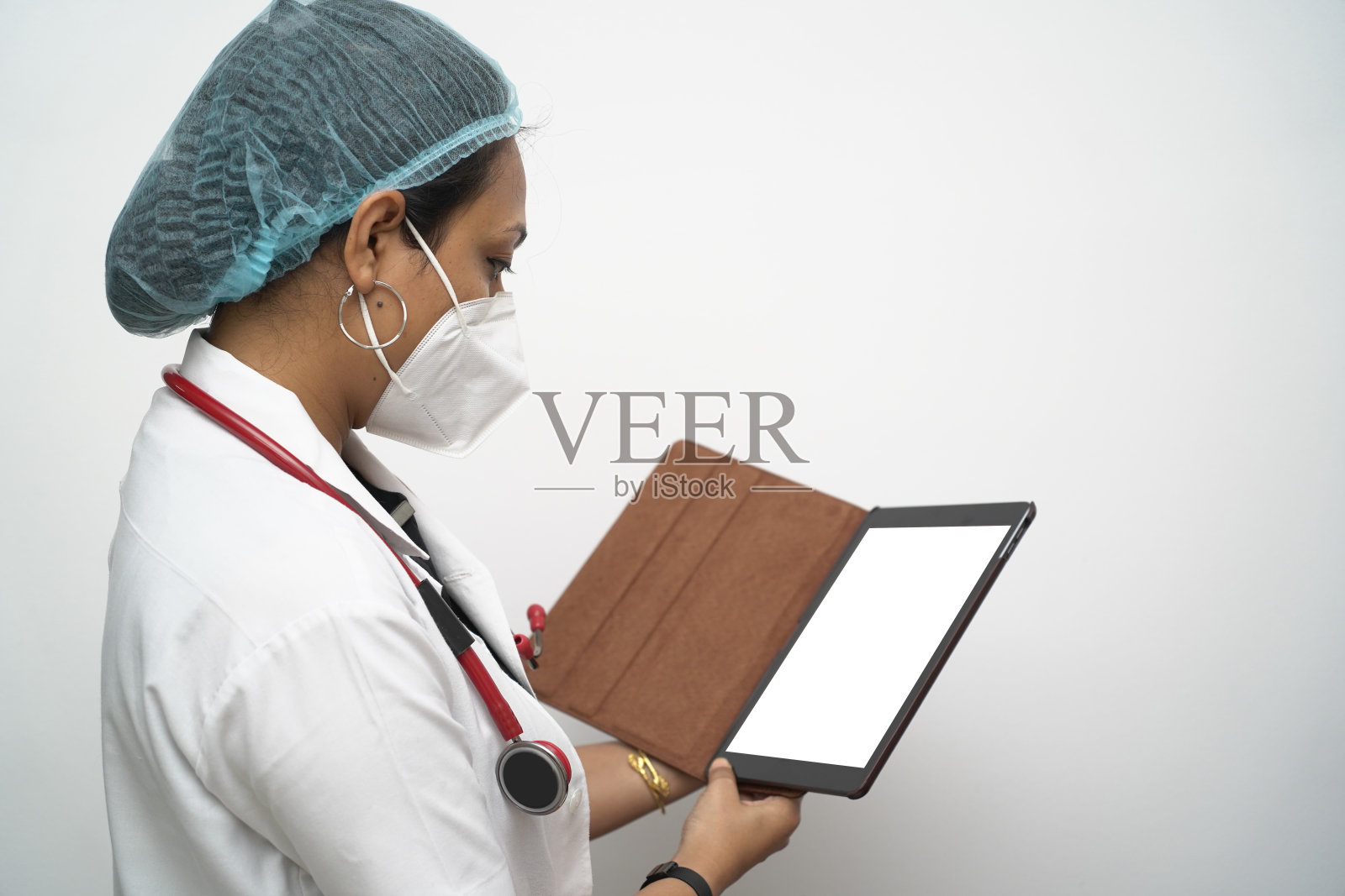 一名30多岁的南印度女医生穿着白大褂和白色背景下的红色听诊器检查药片模型。照片摄影图片