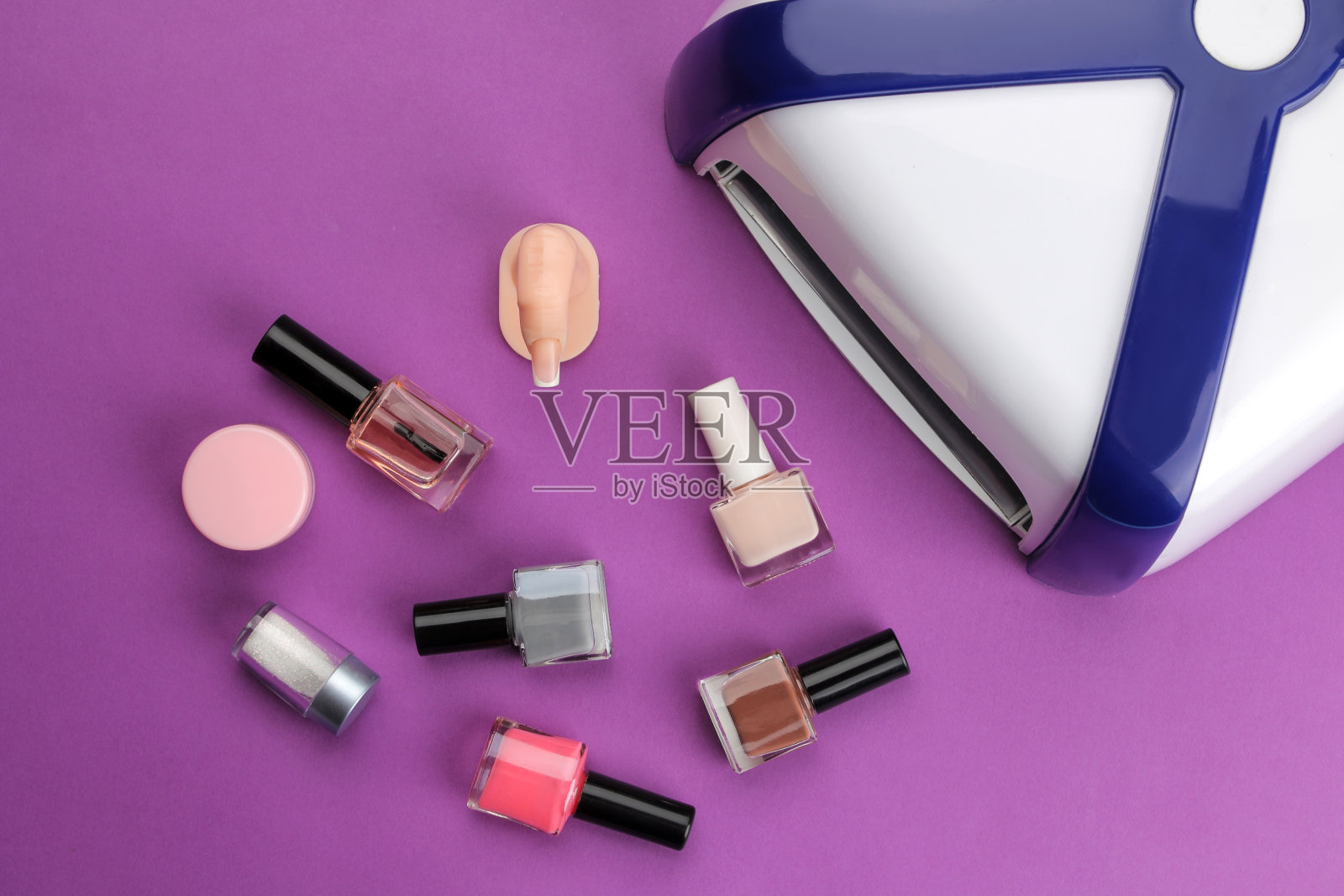 修指甲。紫外线灯和指甲油在一个时髦的紫色背景。美甲配件和指甲工具。俯视图照片摄影图片