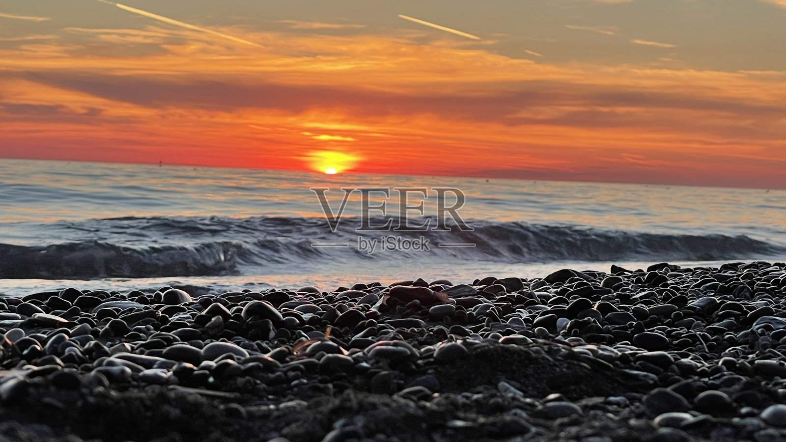 红红的夕阳洒在海面上，有沙、卵石、石子、浪花、太阳、破浪照片摄影图片