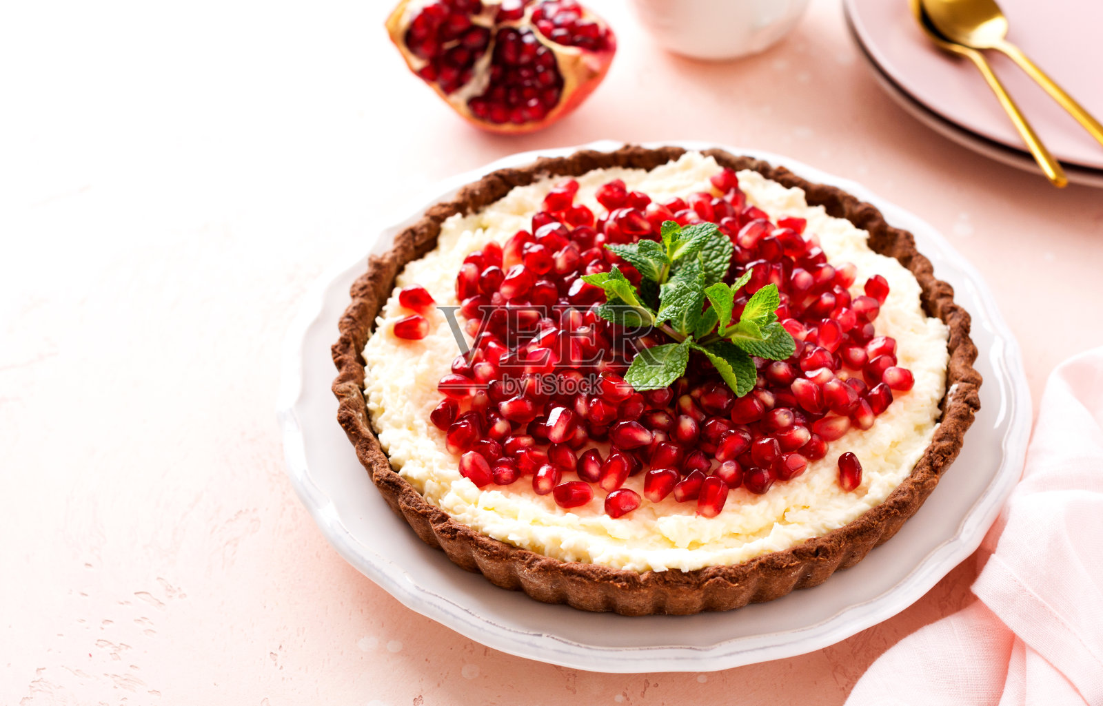 粉红色的桌子背景上有巧克力挞，椰子奶油，石榴和薄荷。自制的甜点。俯视图照片摄影图片