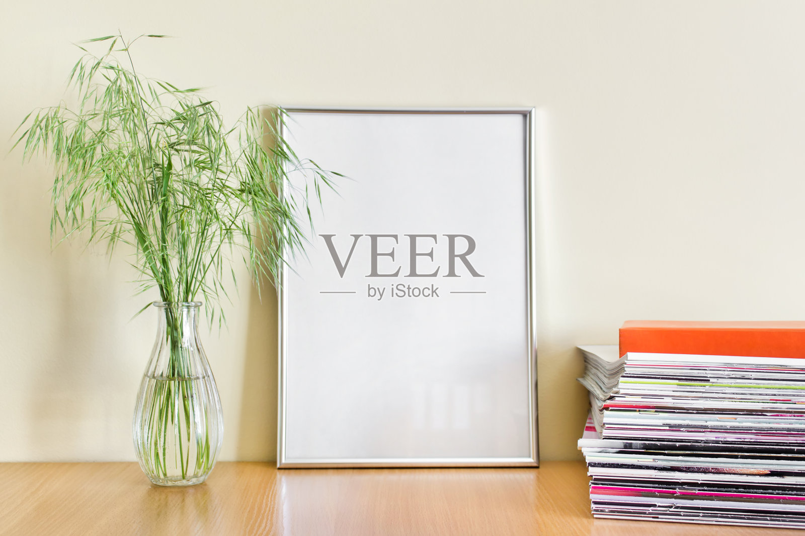 办公室风格的构图与大型空白银色金属A4框架，绿色夏季植物在玻璃花瓶和成堆的杂志照片摄影图片