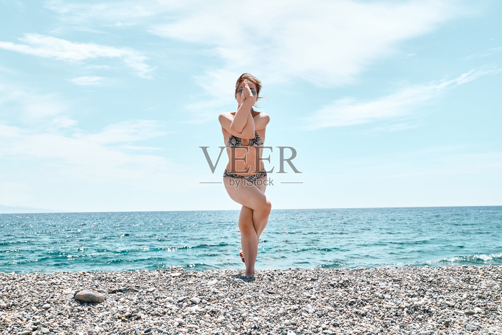 苗条的女人站着做鹰式，老鹰在海滩上摆姿势，蓝色的大海为背景。加强腿部肌肉和身体的协调性。在户外练习瑜伽。照片摄影图片