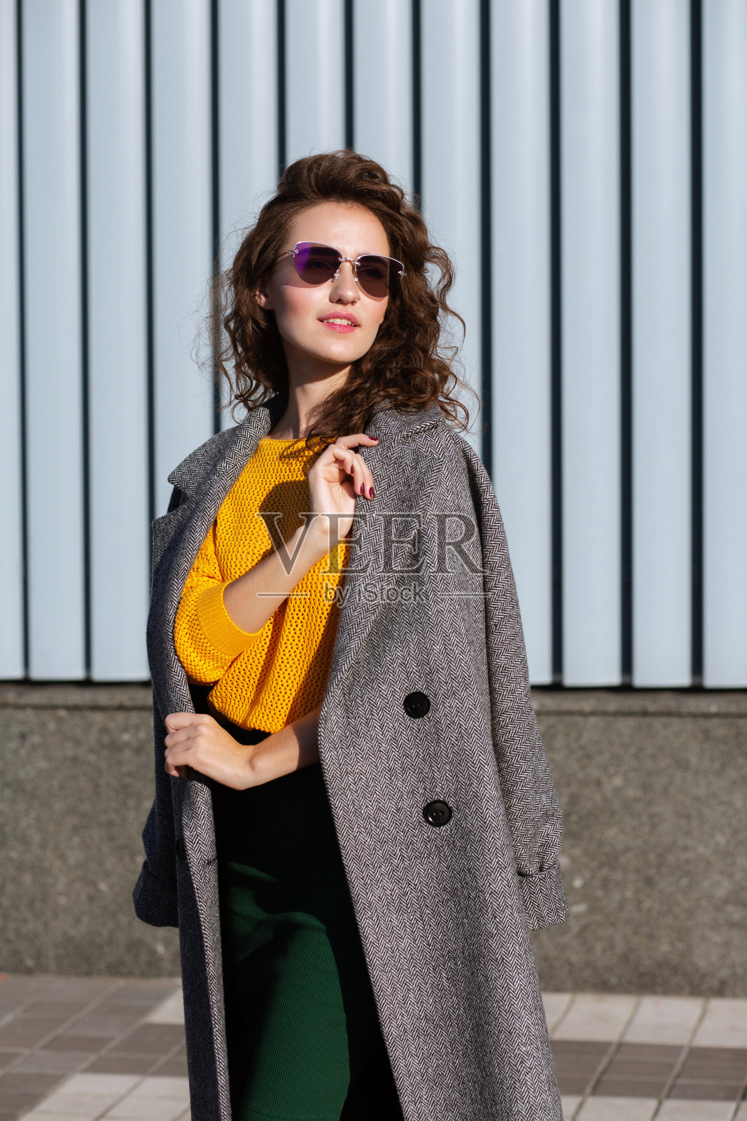 街头时尚模特戴着太阳镜和外套，在城市的百叶窗附近摆姿势照片摄影图片