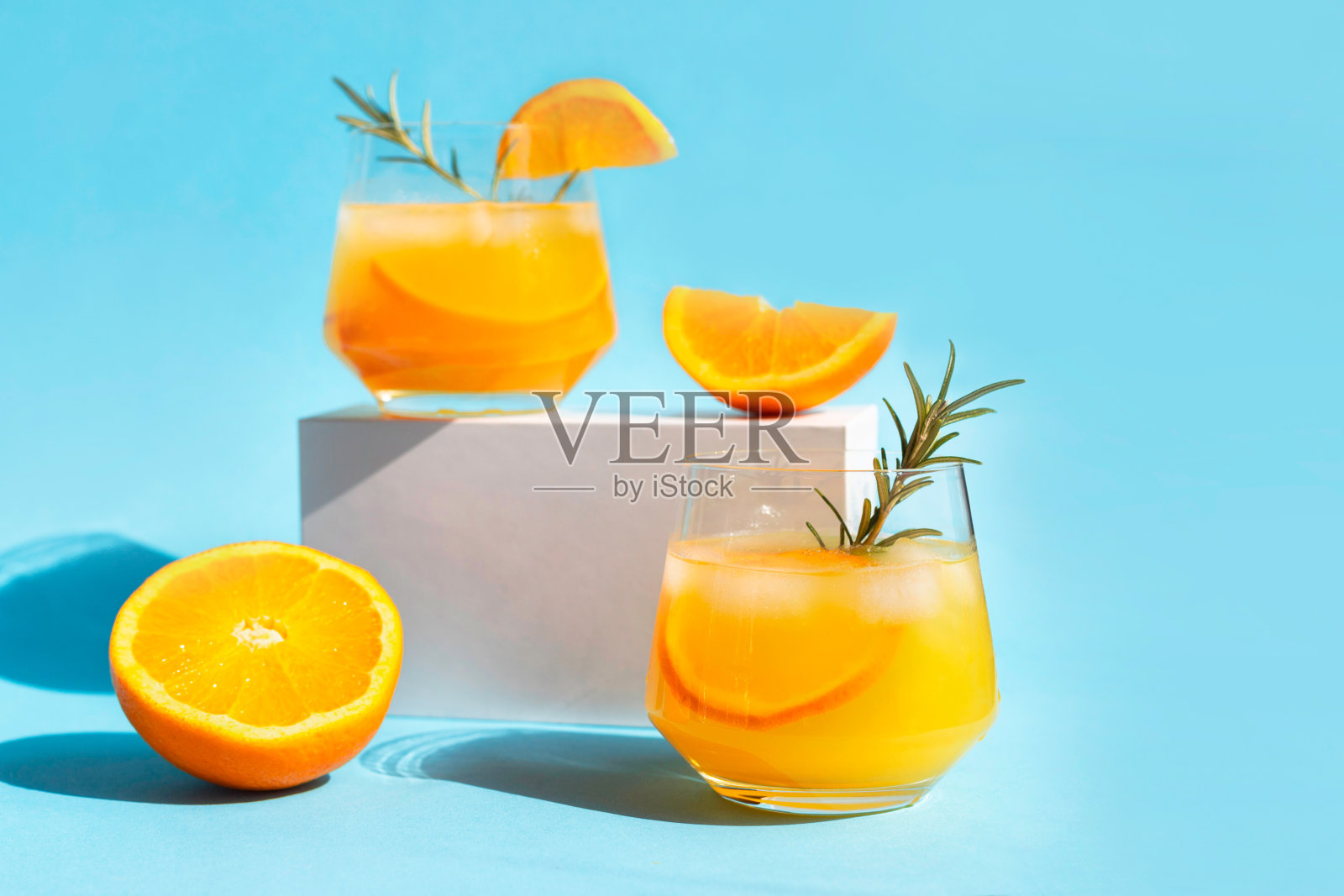 热门饮料。柠檬水，橙汁鸡尾酒，清凉的夏季饮料，加冰和橙片的玻璃杯，在白色的讲台上放一枝迷迭香。照片摄影图片
