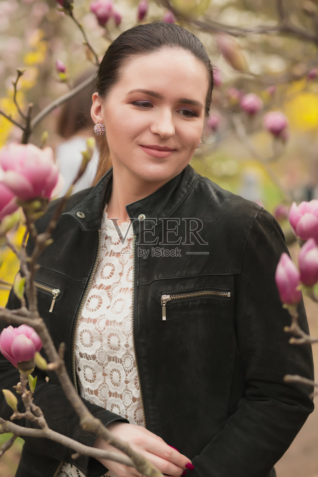 奇妙的黑发女士与化妆，穿着蕾丝衬衫，摆姿势附近盛开的木兰花照片摄影图片