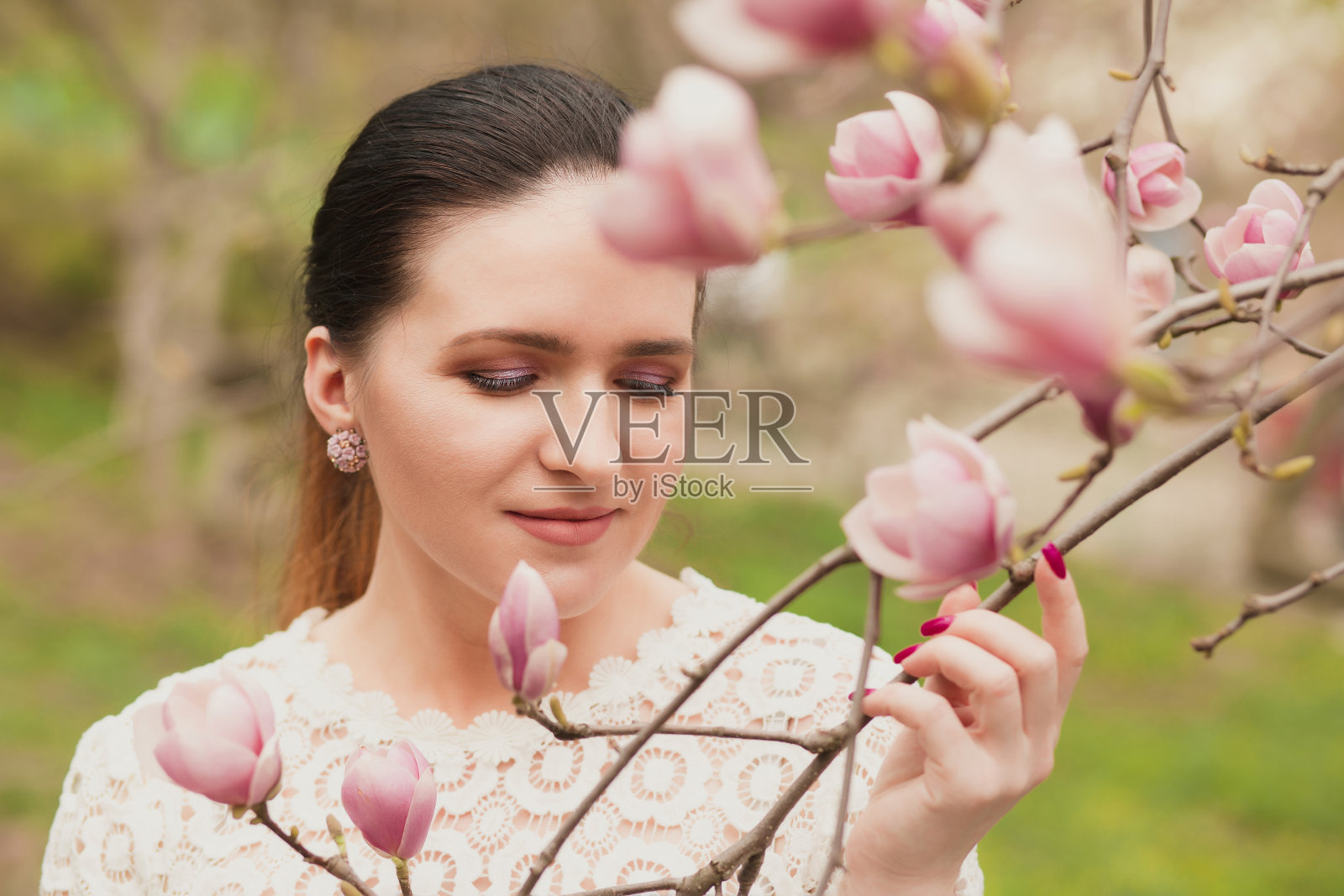 迷人的黑发模特与化妆，穿着蕾丝衬衫，摆姿势附近盛开的木兰花照片摄影图片