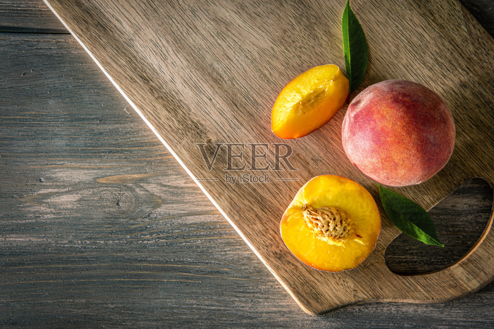 甜美的熟透多汁的桃子和绿色的叶子在木的背景上照片摄影图片
