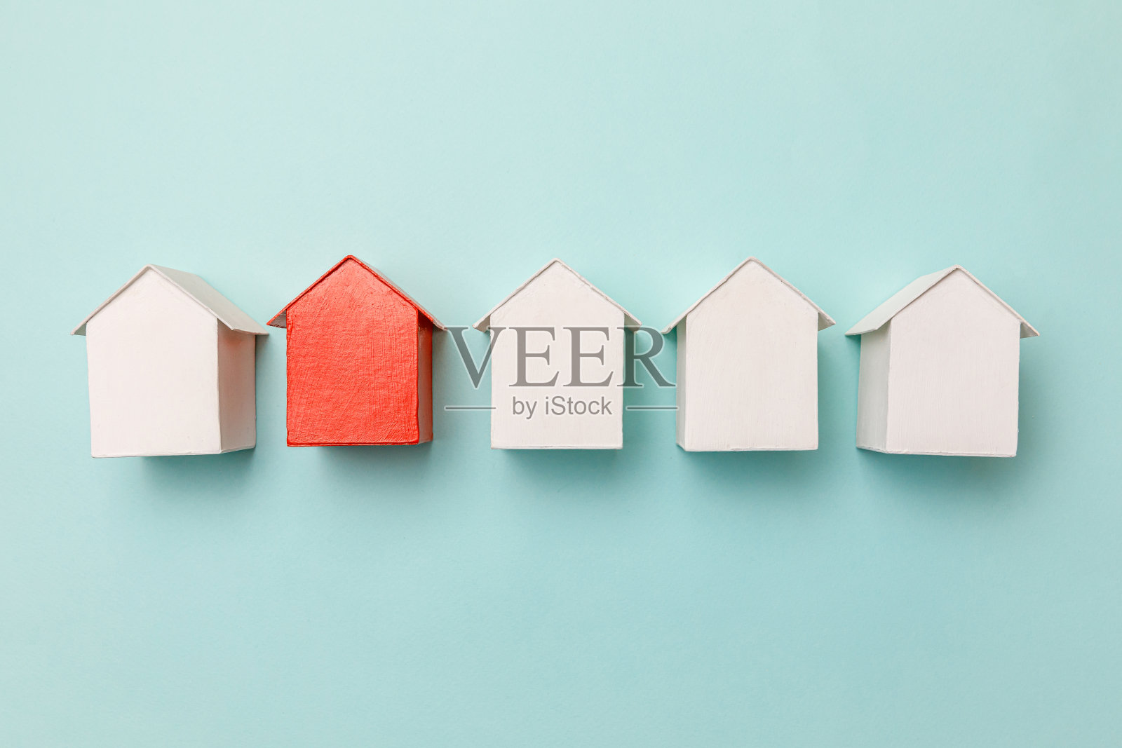 简单的平铺设计与微型的红色玩具模型房子之间的白色房子孤立在柔和的蓝色背景。房地产行业。社区独特的社区选择理念照片摄影图片