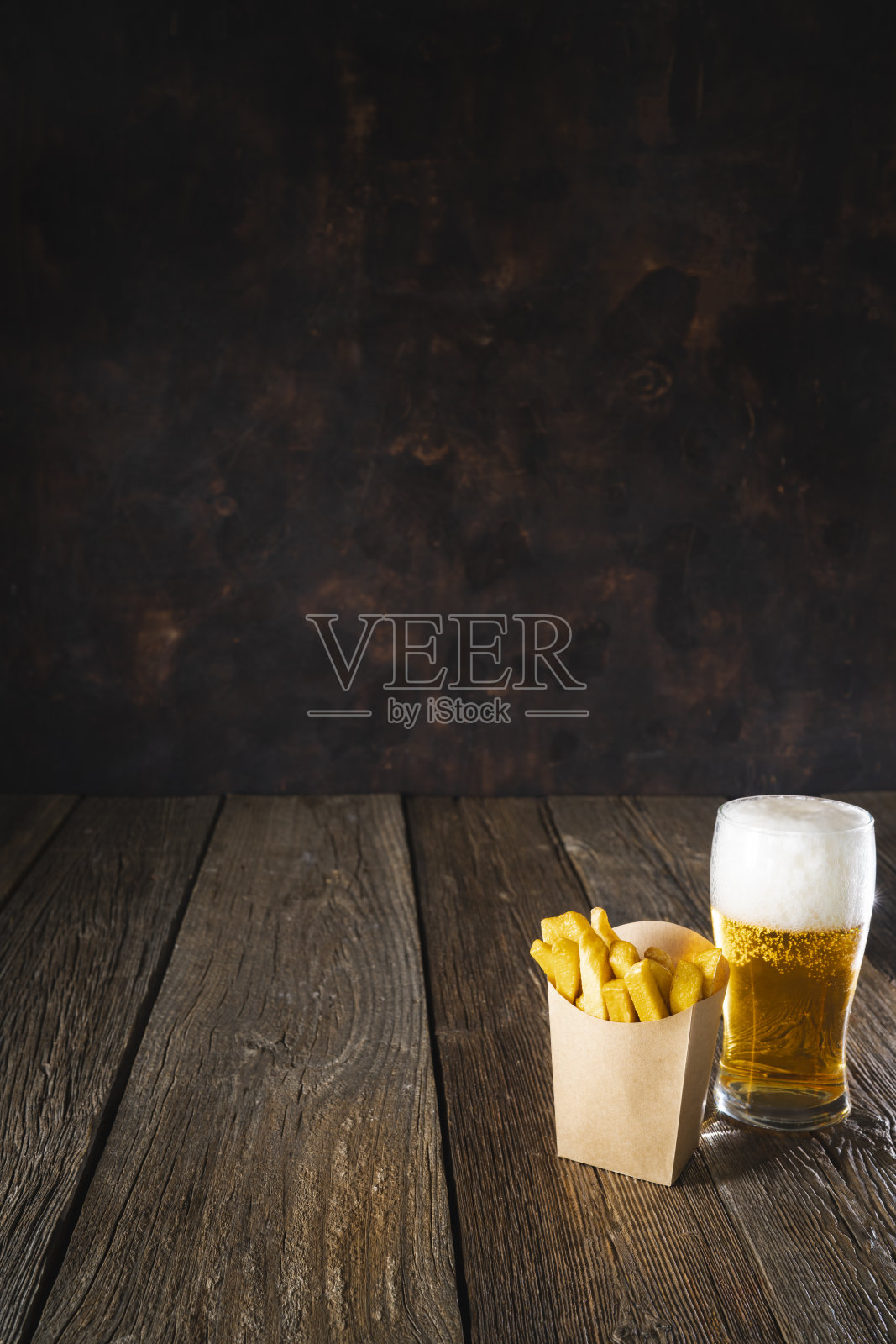 啤酒杯和牛皮纸盒子里的一次性薯条放在深色木桌上照片摄影图片