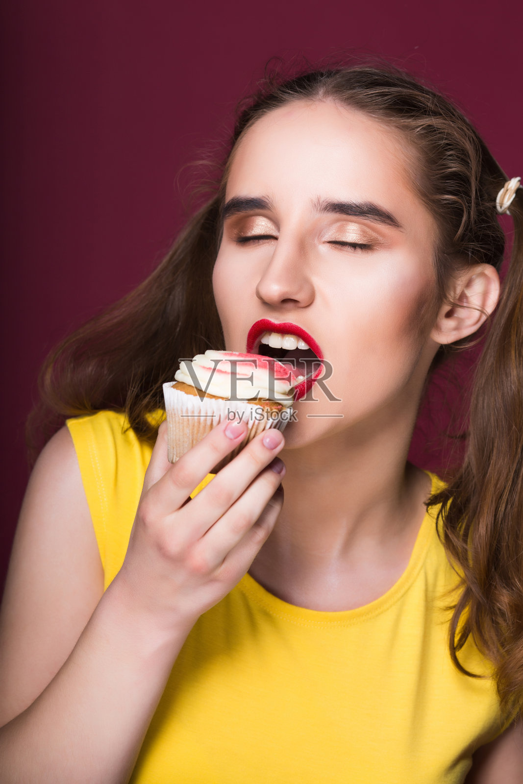 饥饿的黑发模特咬美味的蛋糕与奶油在一个红色的背景照片摄影图片