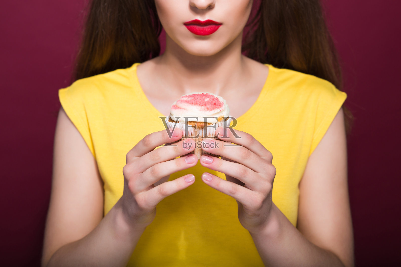 近距离拍摄的年轻的黑发女人与红色的嘴唇持有美味的纸杯蛋糕与奶油照片摄影图片