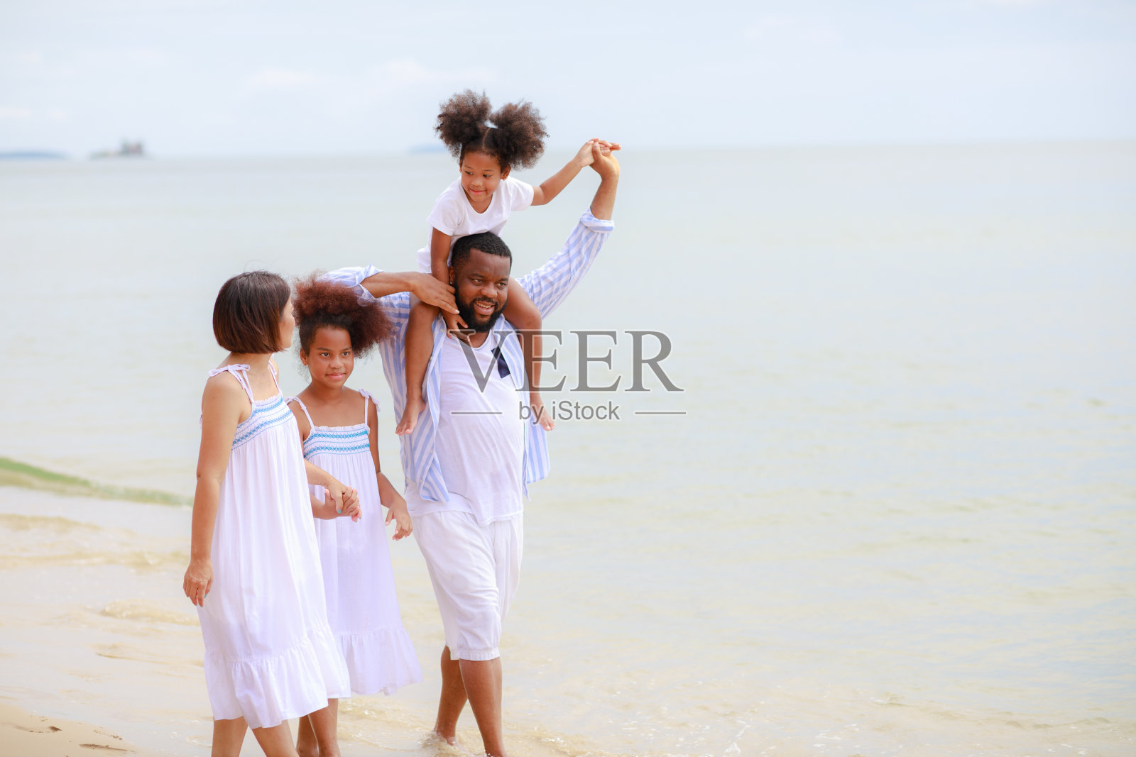 快乐的非裔美国人家庭手牵着手一起在海滩上散步。照片摄影图片