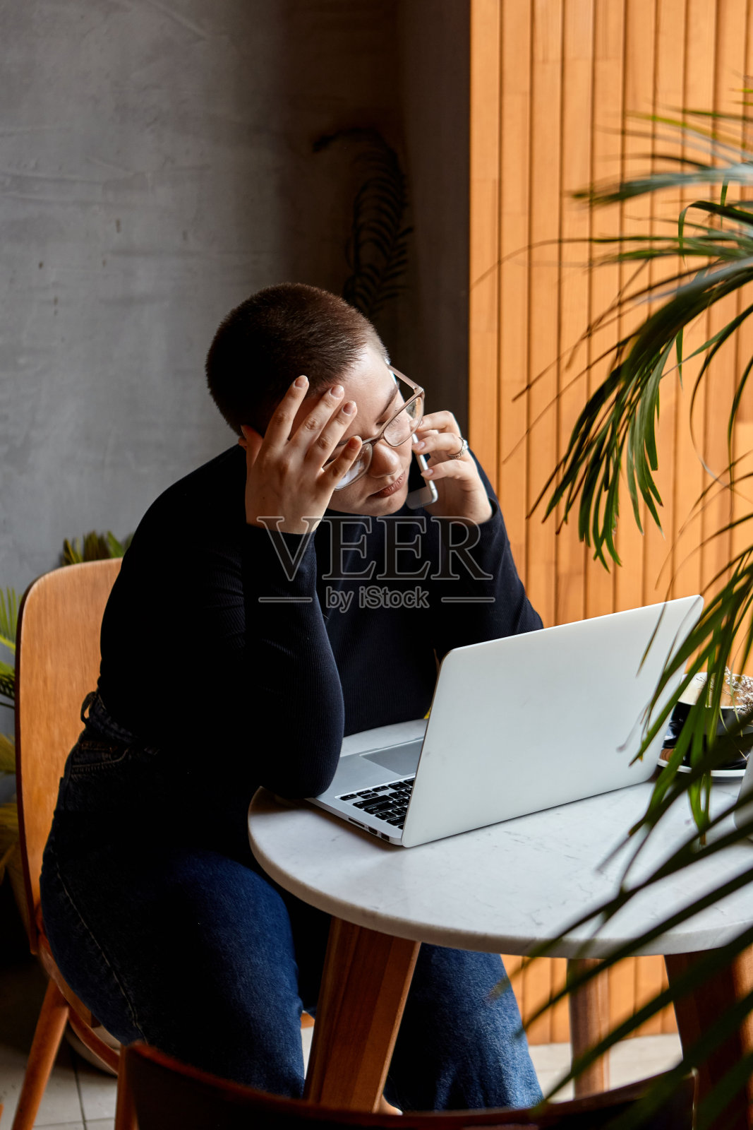 一个留着短发、穿鼻环的年轻女孩坐在咖啡馆里。一个女人一边打电话一边用平板电脑工作。自由职业和远程工作的概念。照片摄影图片