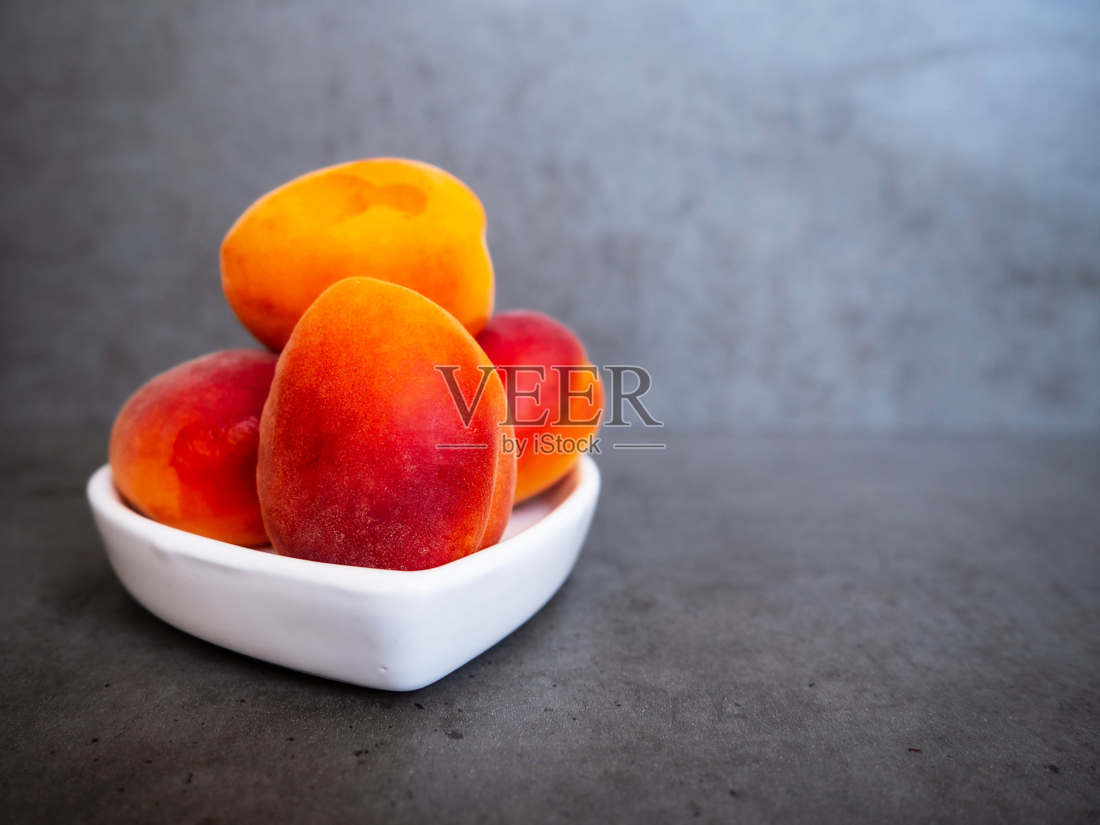 灰色的混凝土桌子上放着一个白色的心型盘子，里面装着美味的成熟的甜杏。水果的背景。照片摄影图片