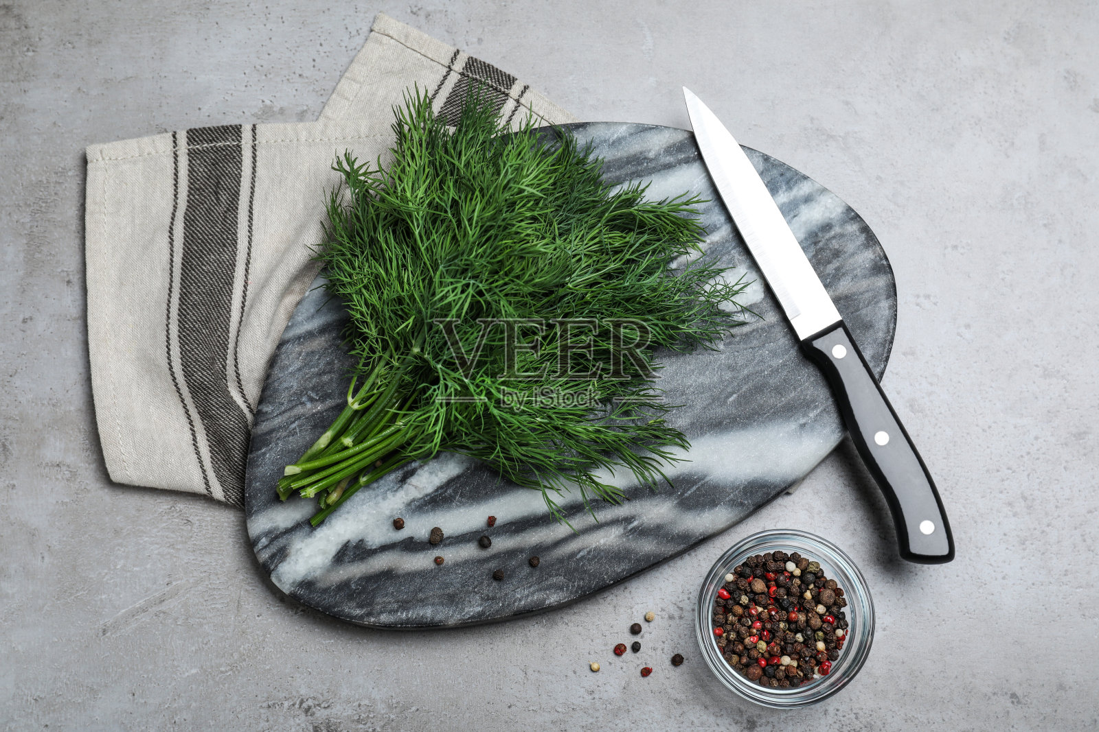 灰色的桌子上放着大理石板，上面放着新鲜的绿色莳萝、小刀和香料照片摄影图片