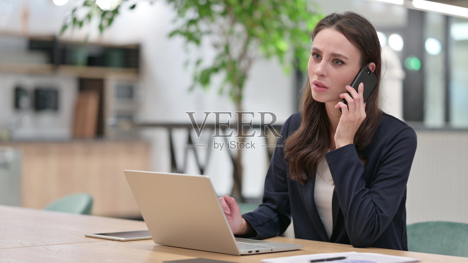 年轻女商人用笔记本电脑在工作时用智能手机聊天照片摄影图片
