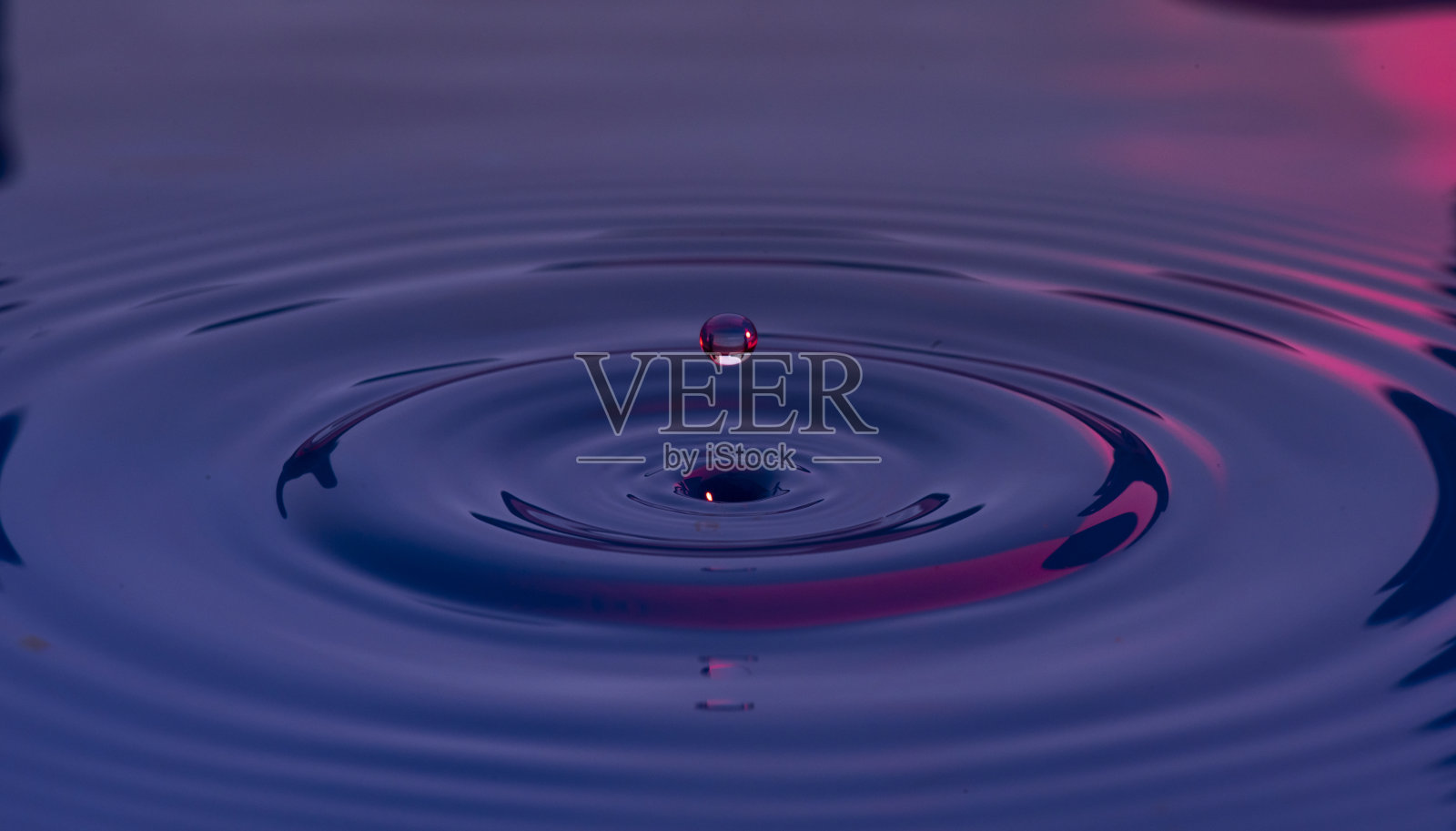 蓝色和紫色的水珠悬浮在空气中，在液体表面形成波浪，代表宁静或宁静照片摄影图片