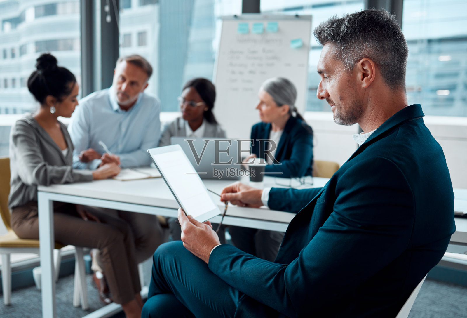 一位成熟的商人在办公室里用着平板电脑，背景是他的同事照片摄影图片