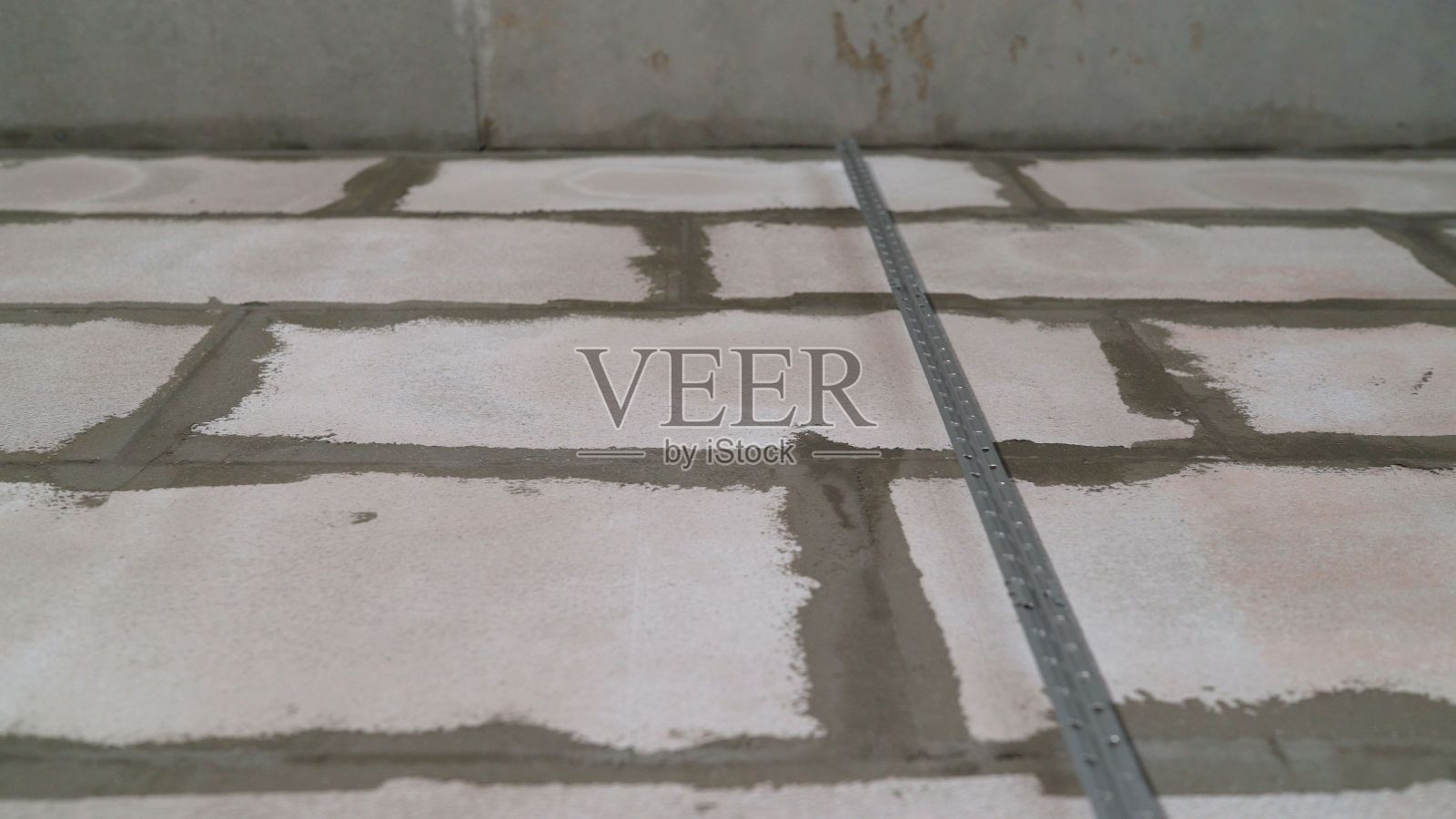 一个金属灯塔安装在混凝土墙上。用金属信标把墙弄平。在砖墙上涂上灰泥。安装金属引导信标，用于修补中墙壁的填充和找平照片摄影图片