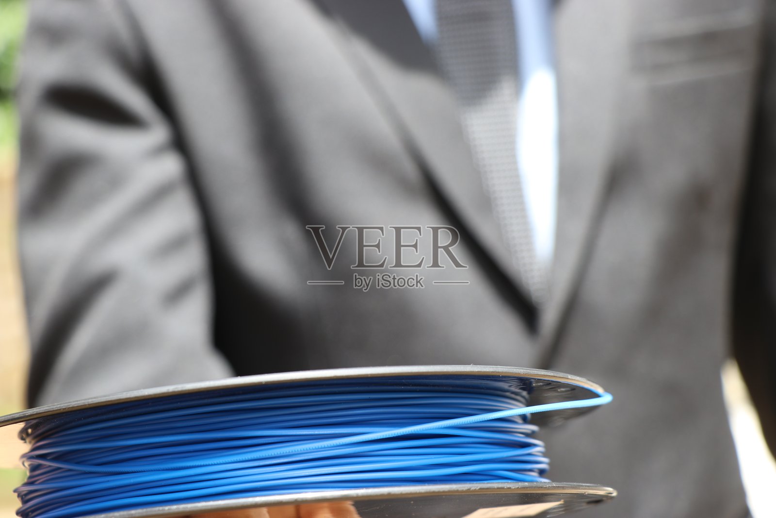 打印机灯丝由西装男手持，展示行业经营理念。PLA长丝是一种热塑性可再生材料照片摄影图片