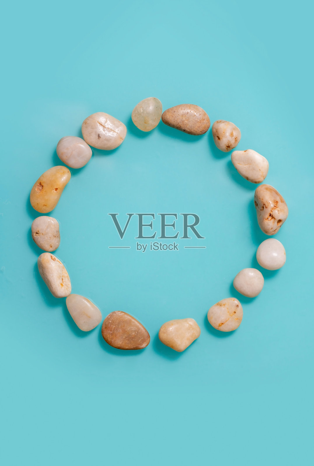 一圈海卵石在一个纯绿松石的背景从上面看。照片摄影图片