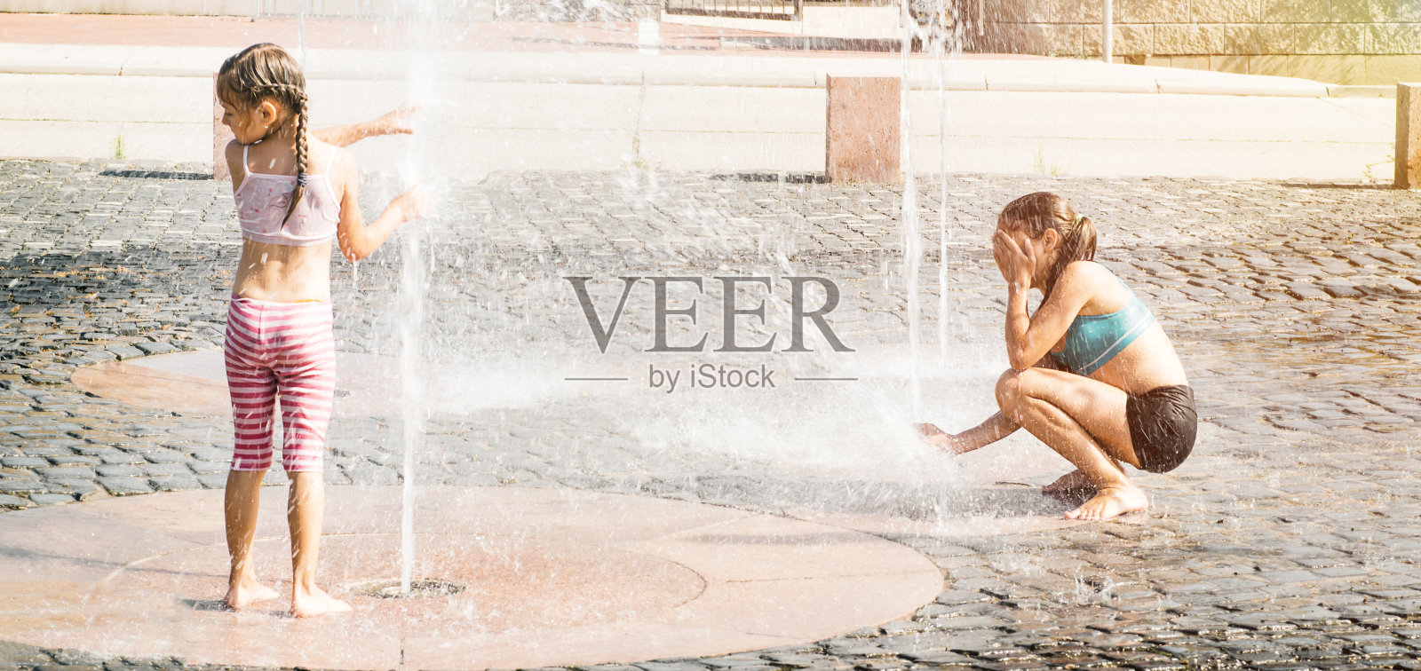 夏天的一天，两个小女孩在喷泉里戏水。夏天热。照片摄影图片