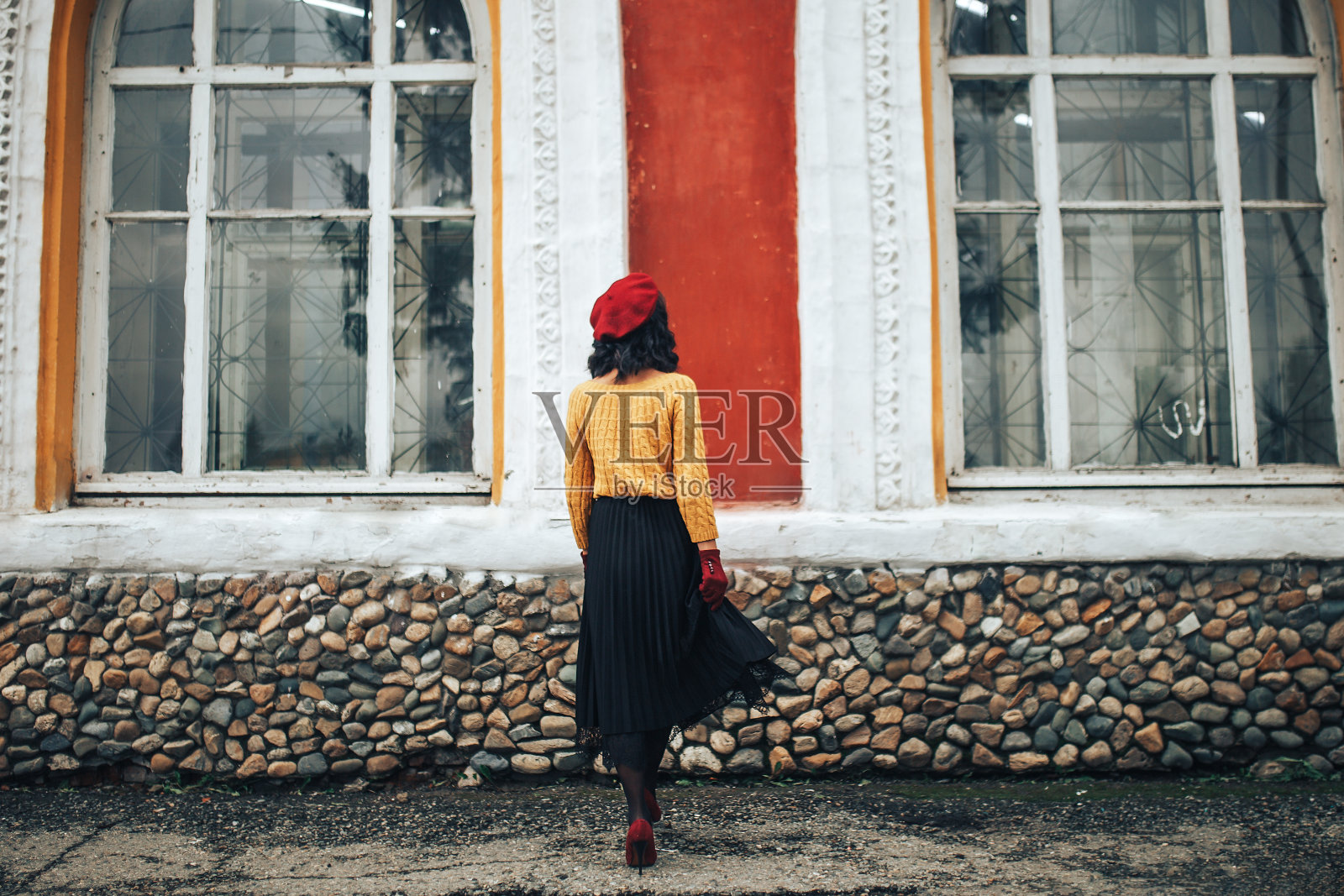 一个穿着黄色毛衣，戴着红色帽子的女人站在一个有大窗户的建筑物的背景下照片摄影图片