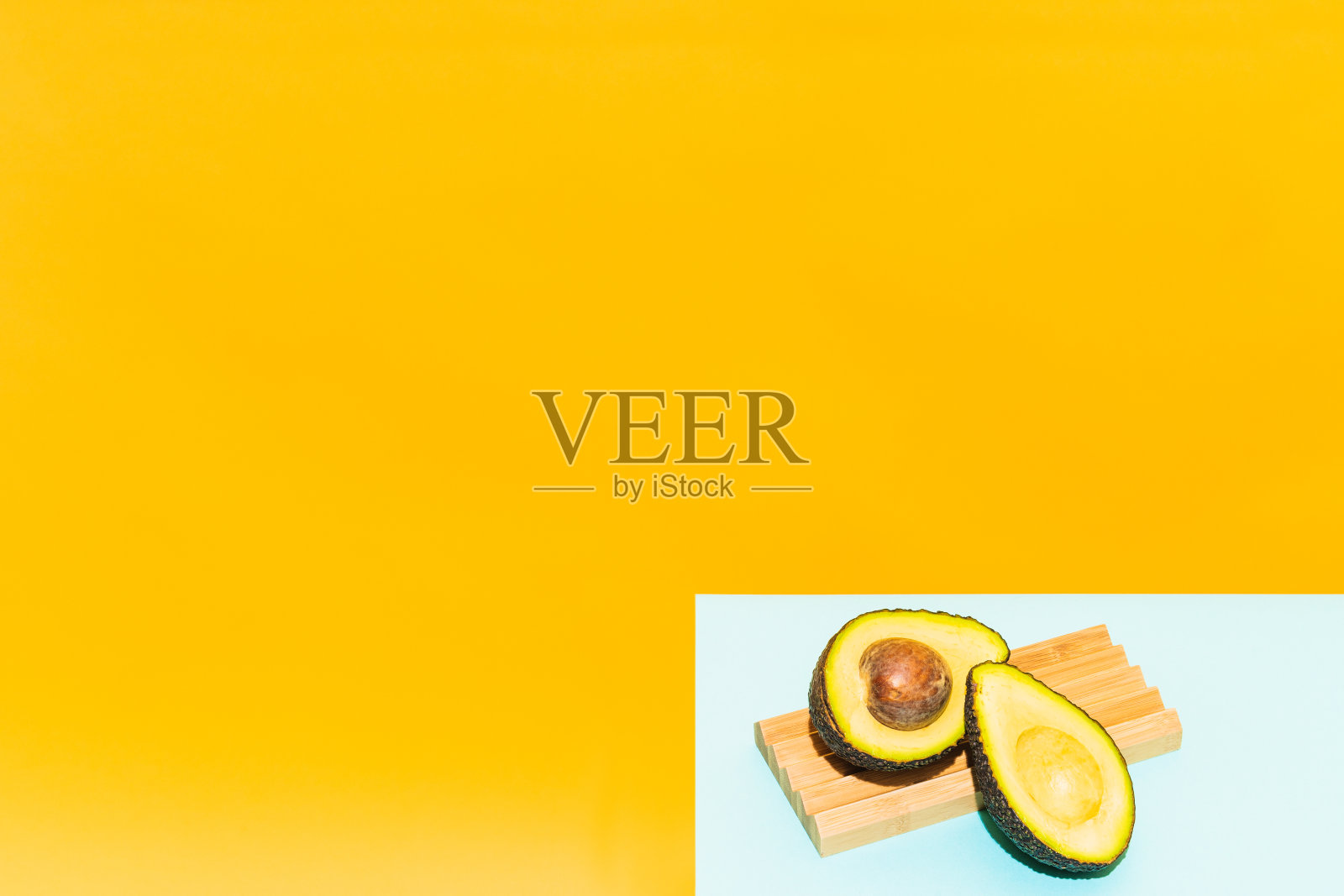 一个切成一半的牛油果，放在木头上，以蓝色和黄色为底色。夏季概念，墨西哥和健康食品。照片摄影图片