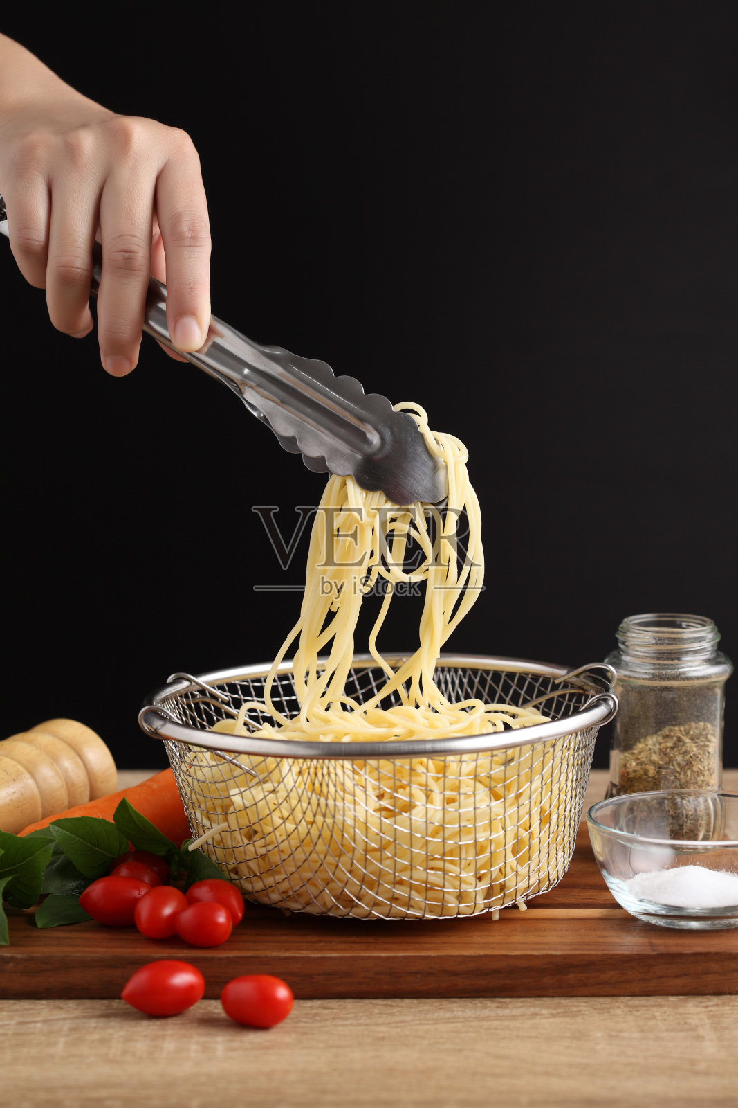 用钳子夹着木头砧板上的金属漏勺煮意大利面照片摄影图片