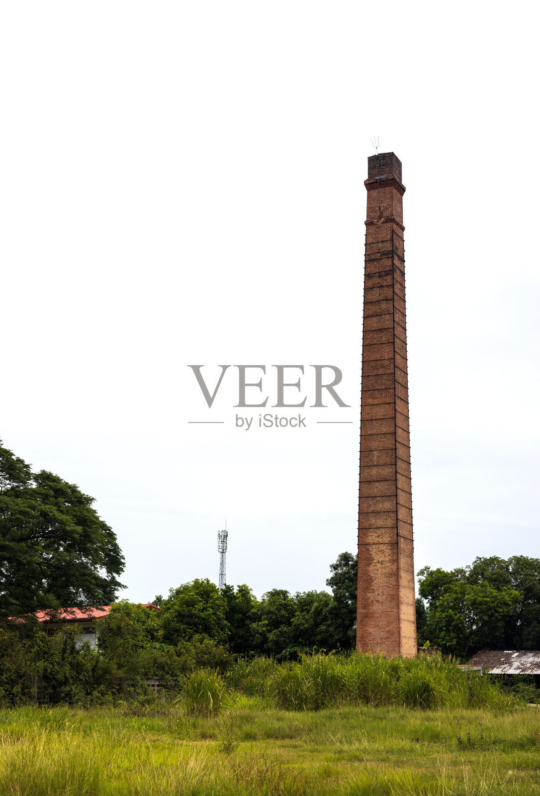 一个古老的砖烟囱高高耸立在农村的草地上。照片摄影图片