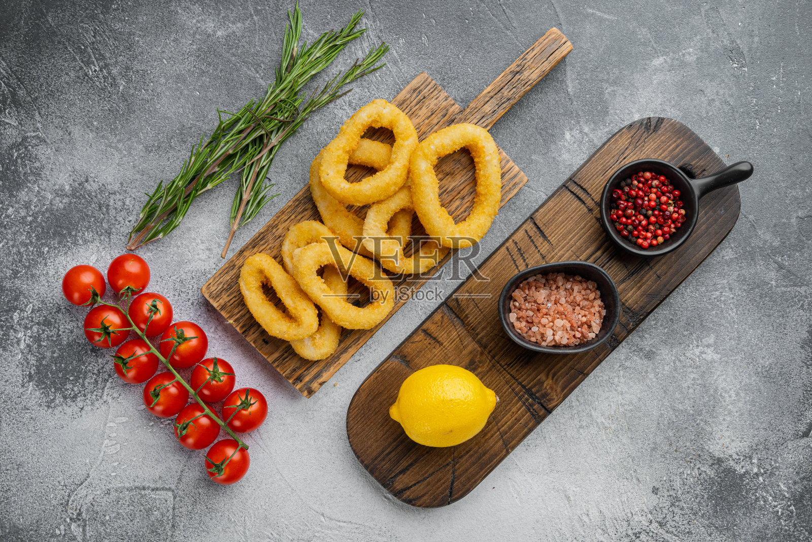 鱿鱼圈或洋葱以面包屑作料，放在上菜板上，放在灰色的石桌背景上，俯视平铺照片摄影图片