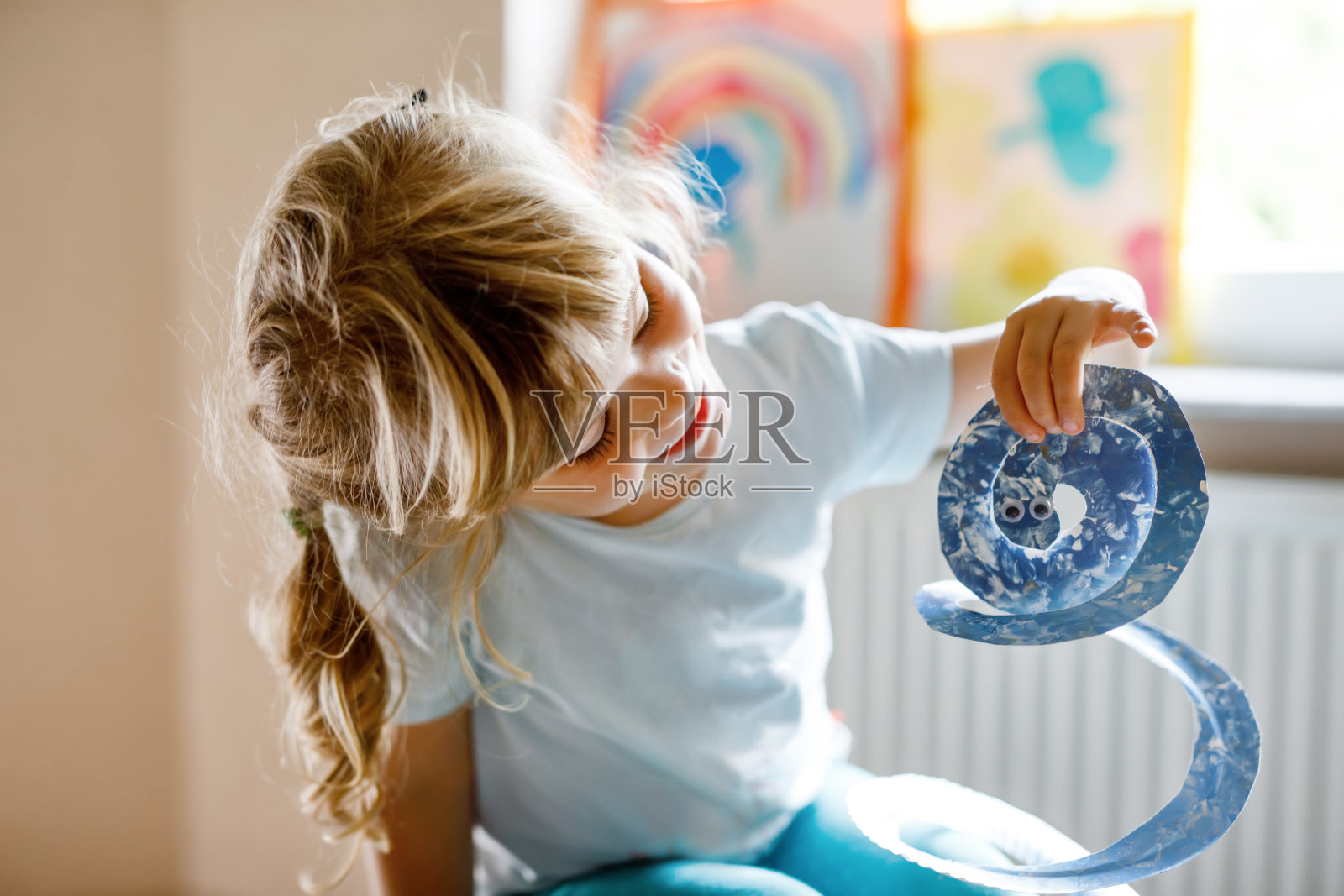 幼稚园的小女孩在家里或托儿所用手指画蛇。室内活动与快乐的创造性幼儿，在家教育与父母照片摄影图片