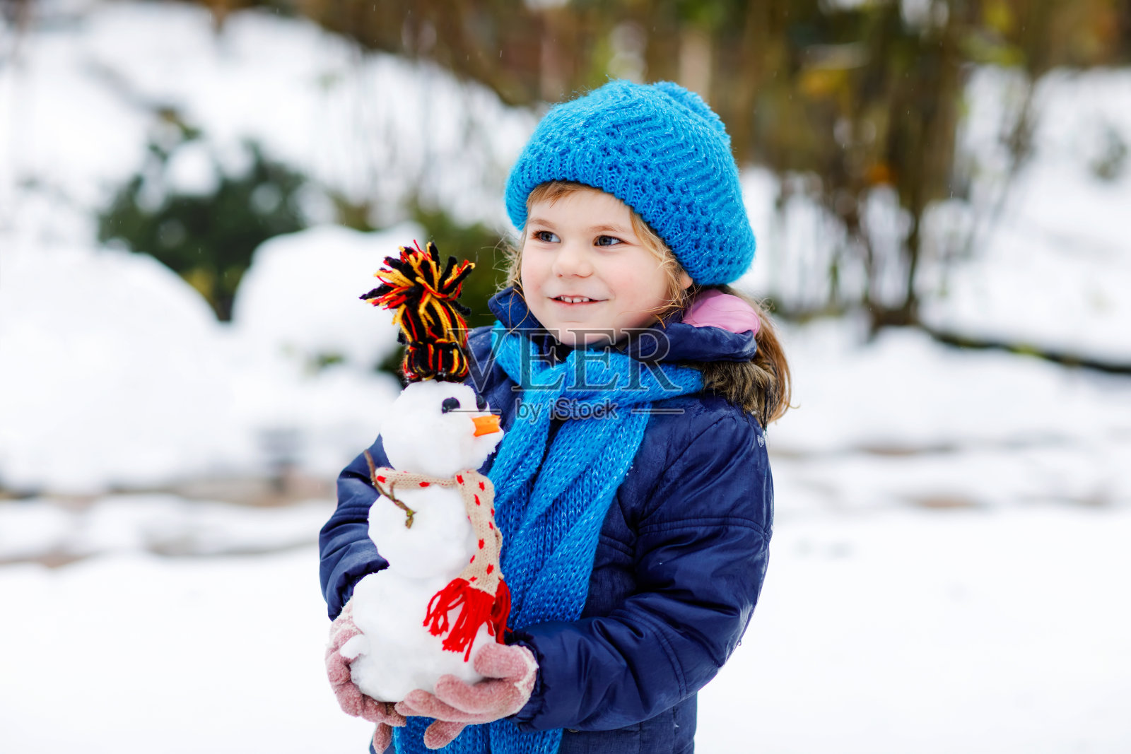 可爱的小女孩做小雪人和吃胡萝卜鼻子。可爱的健康快乐的孩子玩和有乐趣的雪，在寒冷的天户外。在冬季与孩子们积极的休闲活动照片摄影图片