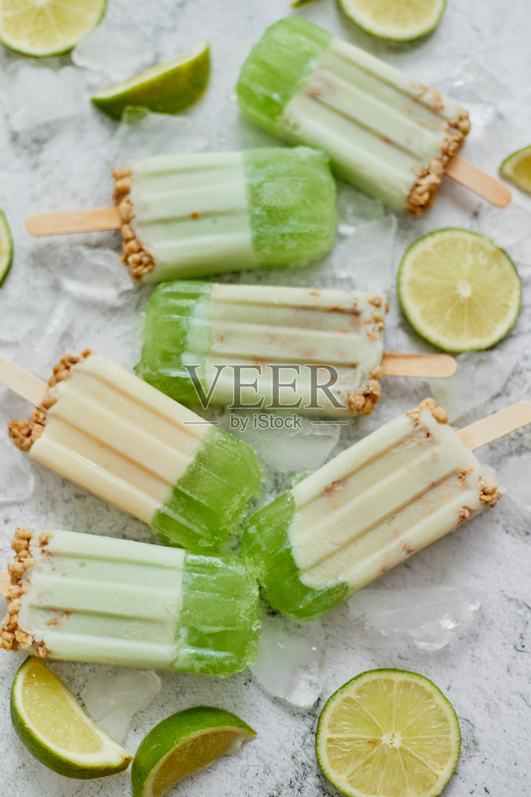 石灰和奶油自制冰棍或冰淇淋与冰块放在灰色的石头背景照片摄影图片