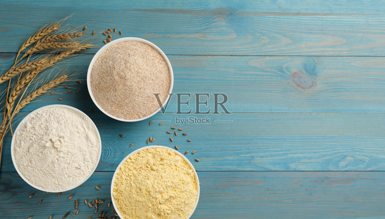 将不同类型的面粉和麦穗放在浅蓝色的木桌上，平铺。空间的文本照片摄影图片