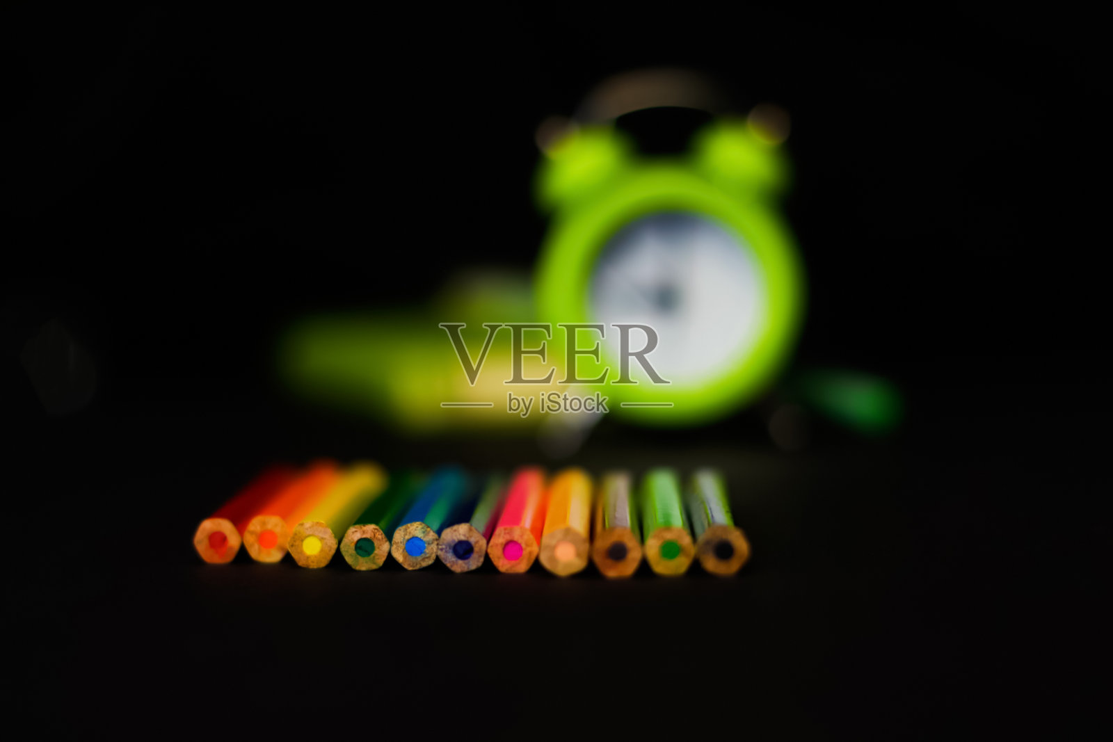 散焦模糊的近距离彩色铅笔与淡绿色闹钟在黑色的背景。画的时候了。艺术学校。的焦点照片摄影图片