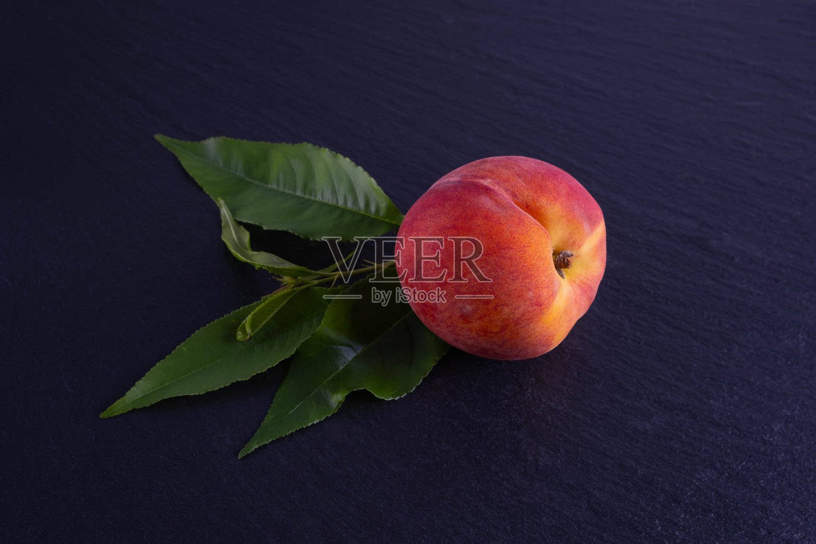 一个桃子和绿色的叶子，躺在一个黑色的背景，特写照片摄影图片