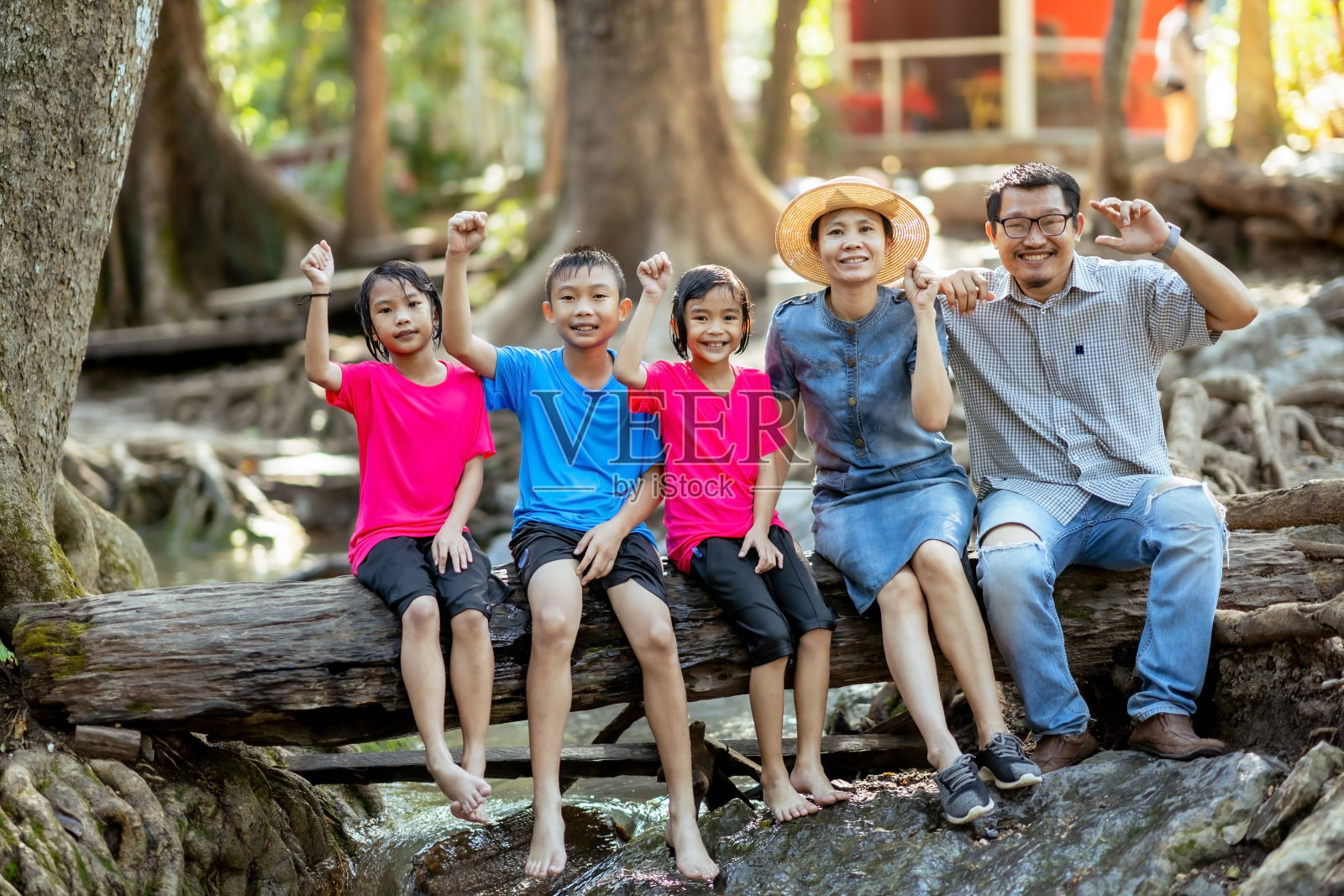 家庭和孩子们坐在自然瀑布的木材或原木上，快乐的家庭在假期放松时间，孩子们在自然瀑布中玩耍和学习，夏季亚洲家庭旅游照片摄影图片
