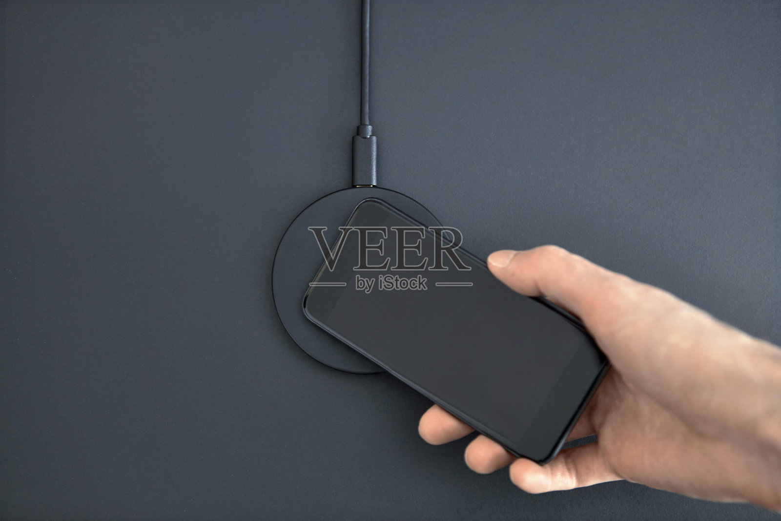 男性将智能手机放在无线充电器上给电池充电。圆形设备摆放在办公桌上。照片摄影图片