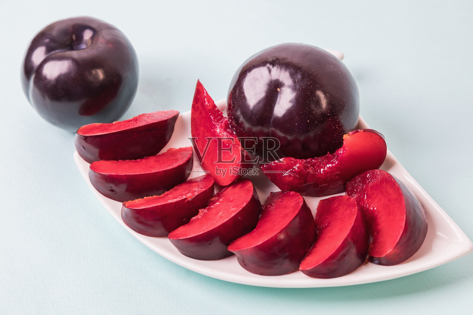 在一个白色的碟子上有一个切成楔形的大李子，旁边还有两个李子。照片摄影图片