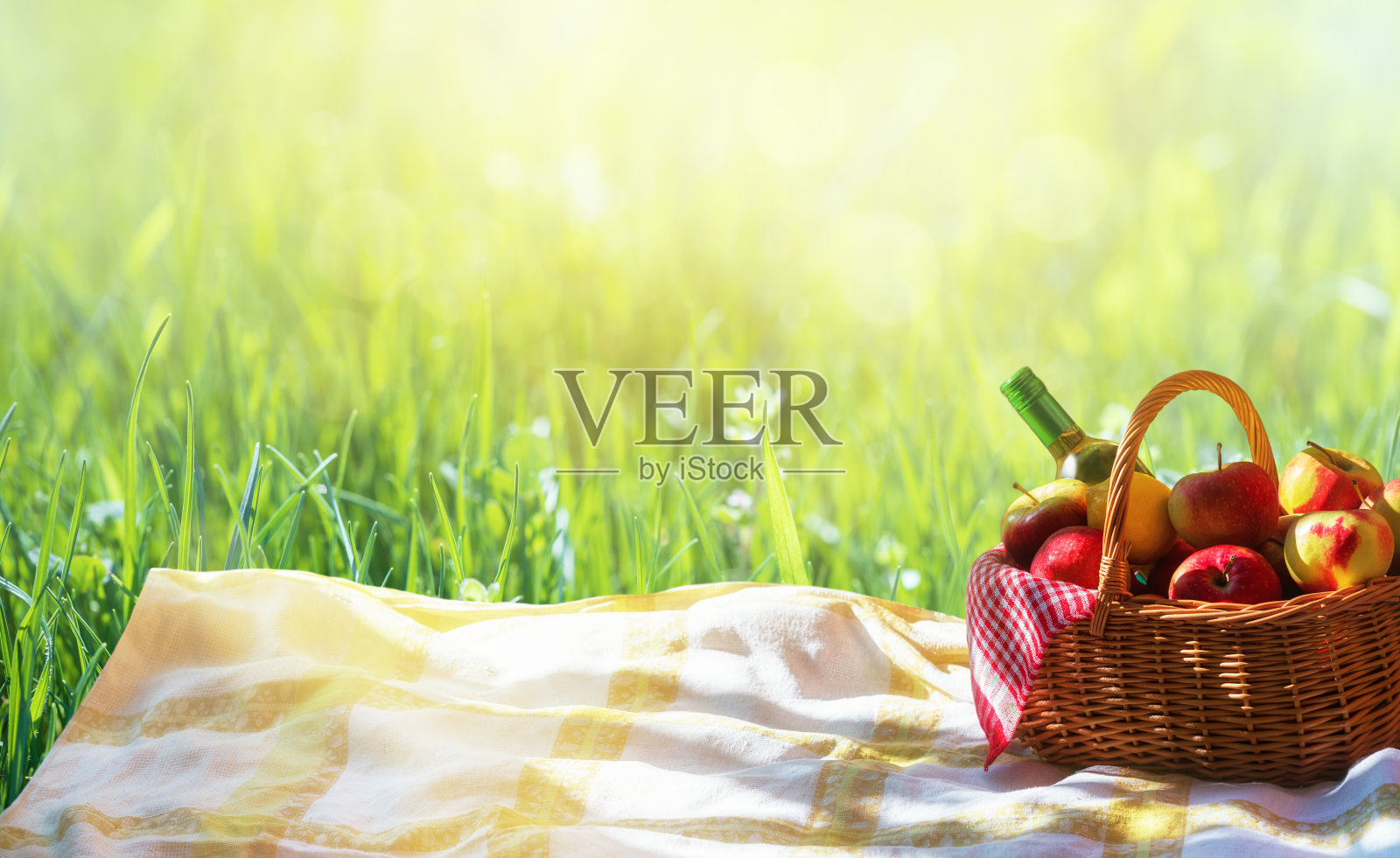 草地上放着一篮子苹果和苹果汁或葡萄酒。带酒和水果篮的户外野餐。照片摄影图片