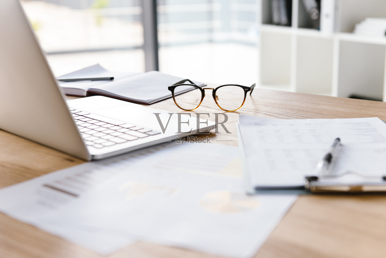 在一个没有人的办公室里，打开笔记本电脑，剪贴板，眼镜，铅笔和笔记本躺在木桌上照片摄影图片