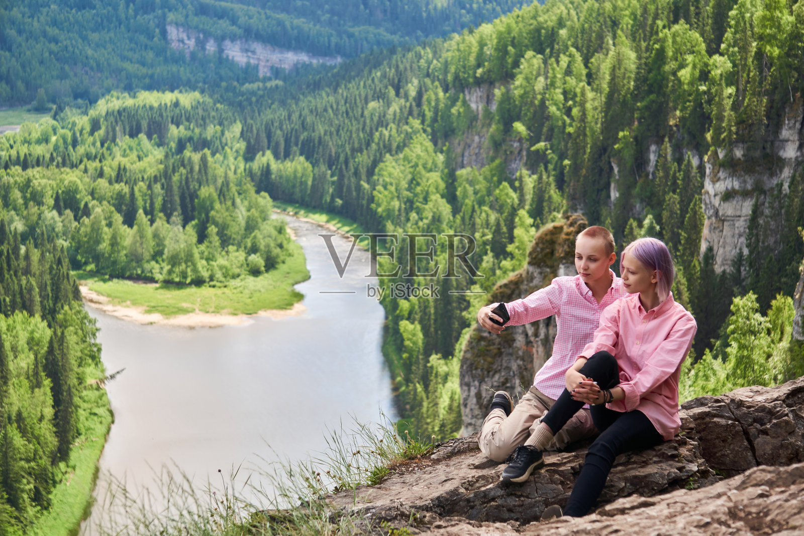 两名少女在河上的悬崖边自拍，背景是自然景观照片摄影图片