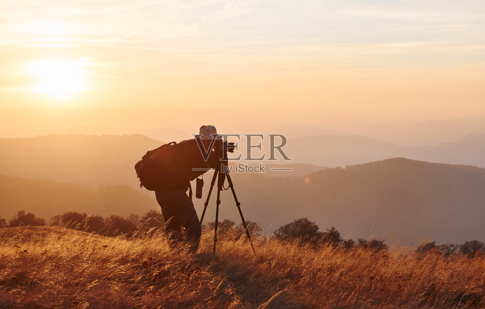 男摄影师站在和工作在雄伟的景观秋天的树木和山的地平线照片摄影图片