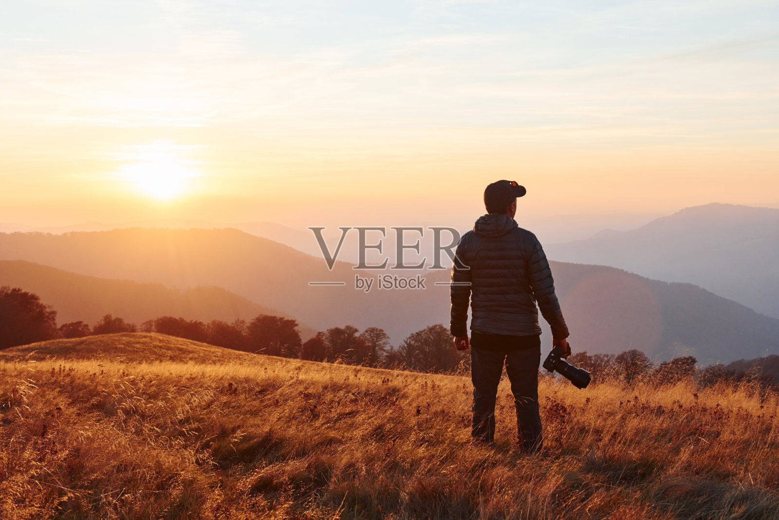 男摄影师站在和工作在雄伟的景观秋天的树木和山的地平线照片摄影图片