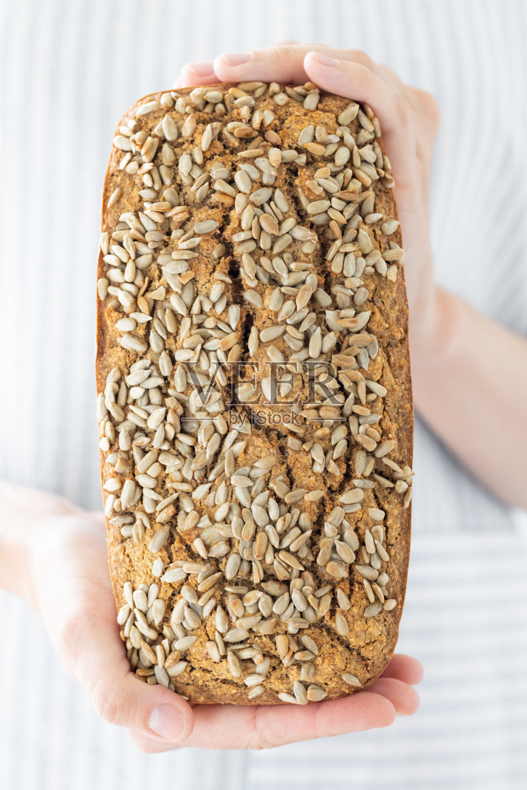 欧洲妇女面包师拿着荞麦面包，白人妇女穿着浅色围裙拿着自制的酸面包照片摄影图片