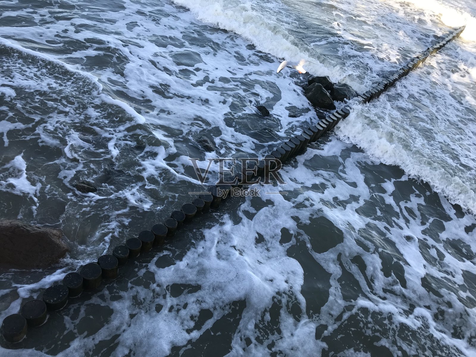 在波罗的海海岸的木制防波堤上破浪。照片摄影图片