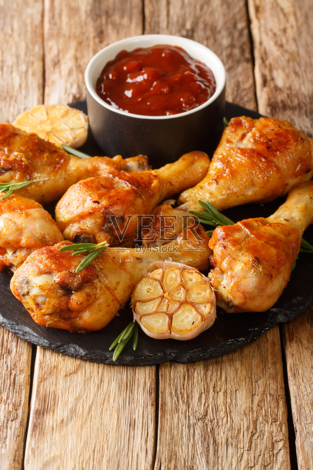 烤鸡腿与大蒜和迷迭香与烧烤酱的特写板。垂直照片摄影图片